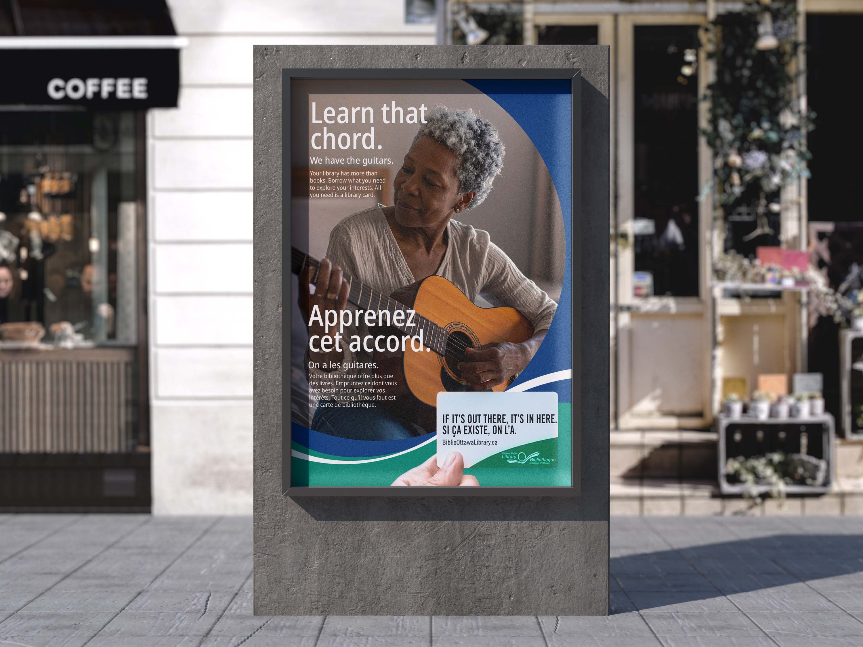 Street poster outside a café: an older woman learning guitar. Learn that chord. We have the guitars. Apprenez cet accord. On a les guitares. A hand holds out an Ottawa Public Library card.