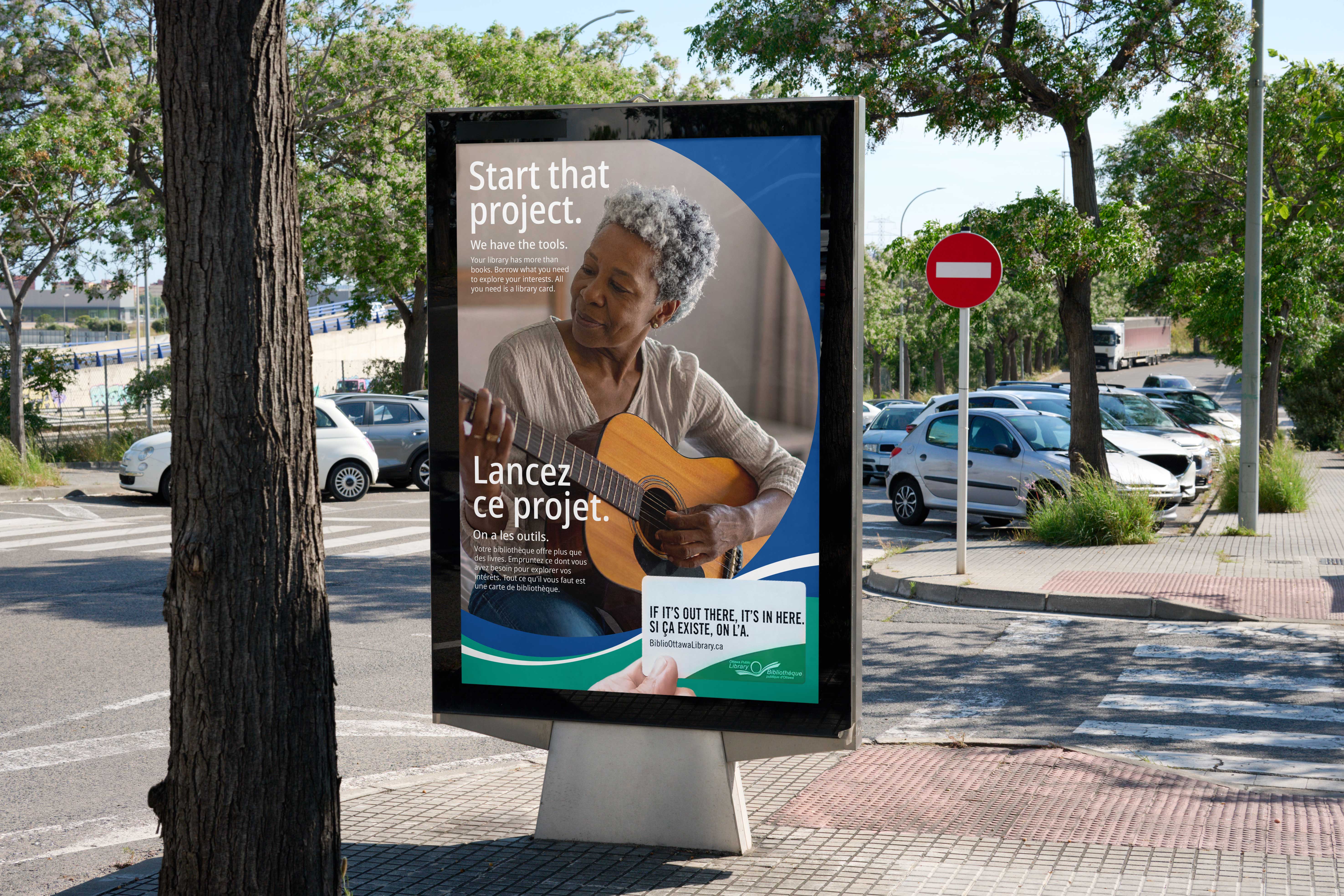 Street-level poster showing older woman playing guitar with 'Start that project' headline in English and French